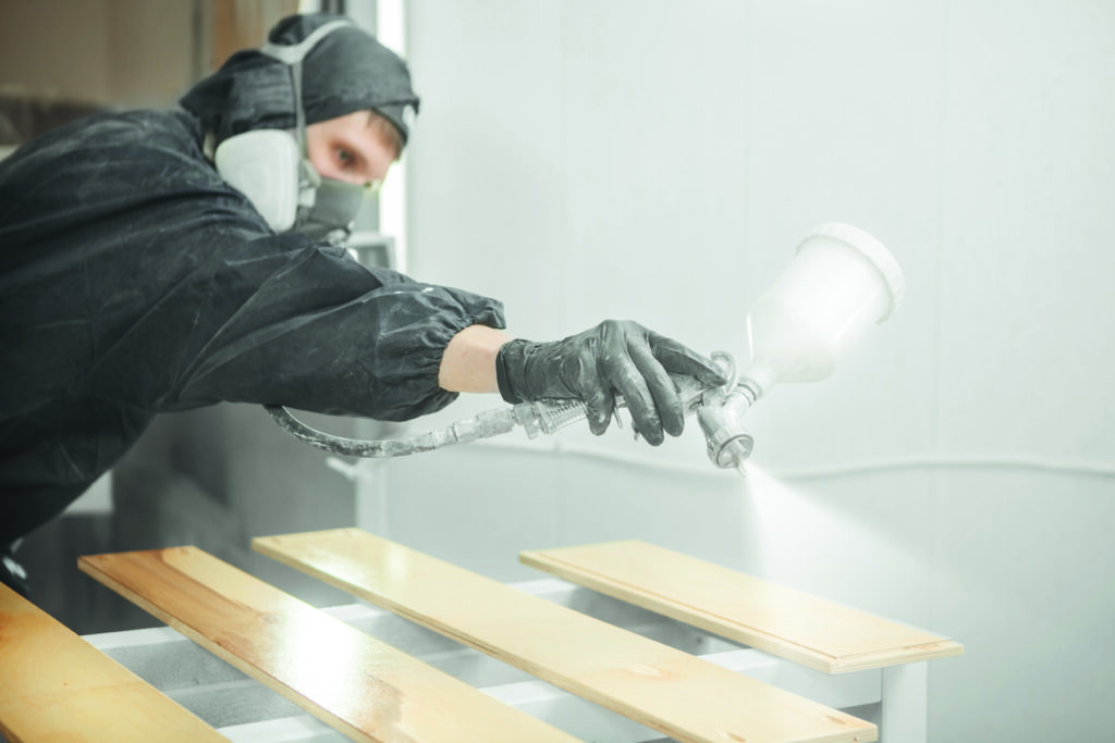 Industrielackierer beschichtet Bauteile aus Holz.