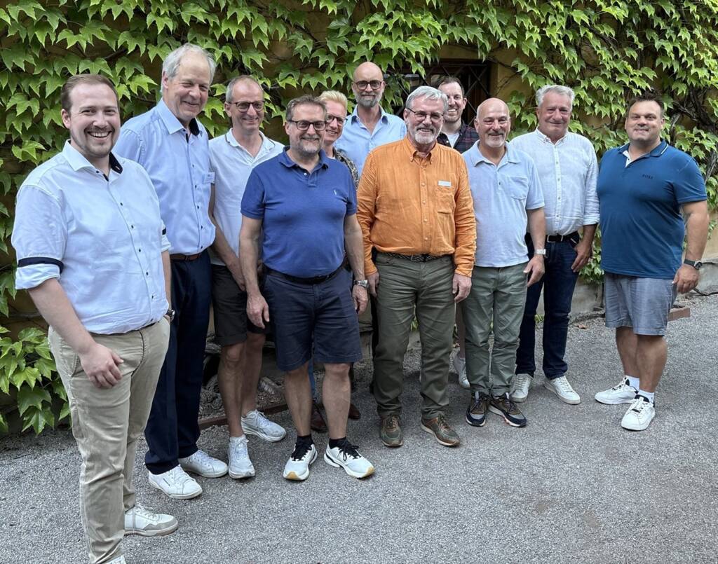 11 Männer stehen vor einer Hecke für ein Gruppenfoto